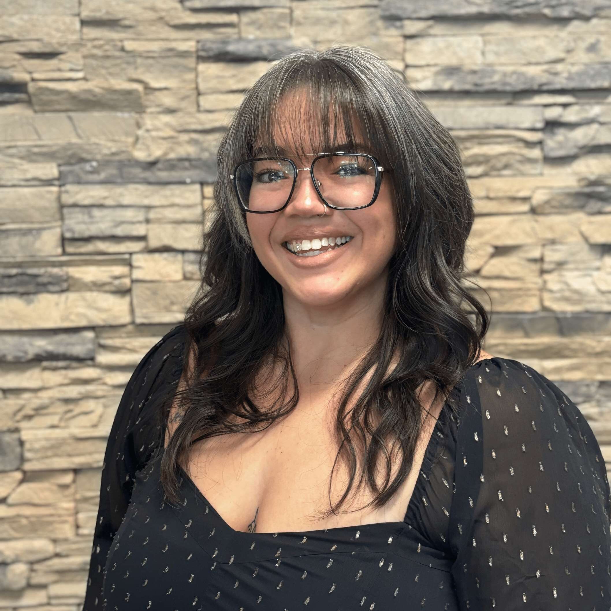 A woman with glasses standing in front of a stone wall.